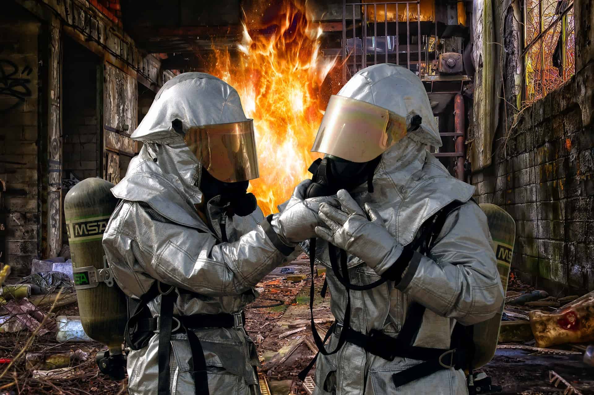 two firemen in flame retardant suits in front of a burning building